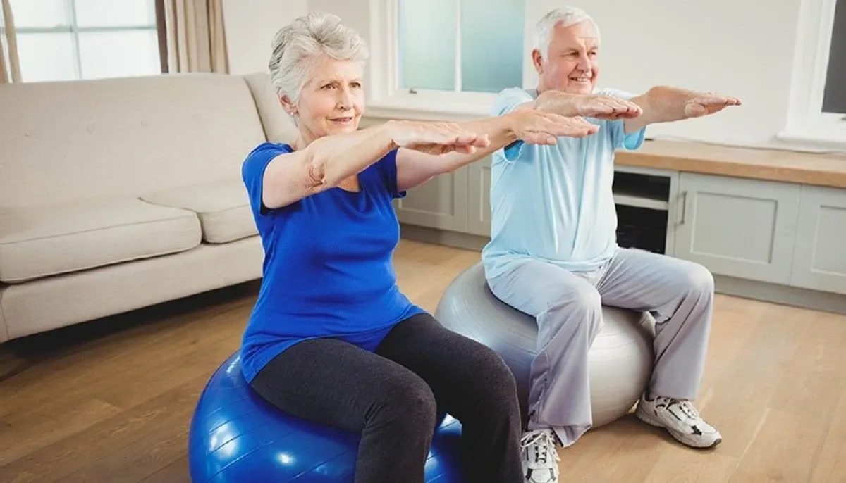 Dos adultos mayores haciendo ejercicios sentados sobre pelotas de pilates