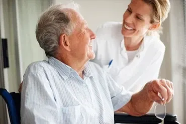 Enfermera sonriendo junto a un hombre mayor en silla de ruedas