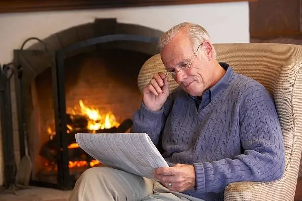 Hombre mayor leyendo el diario junto al fuego del hogar